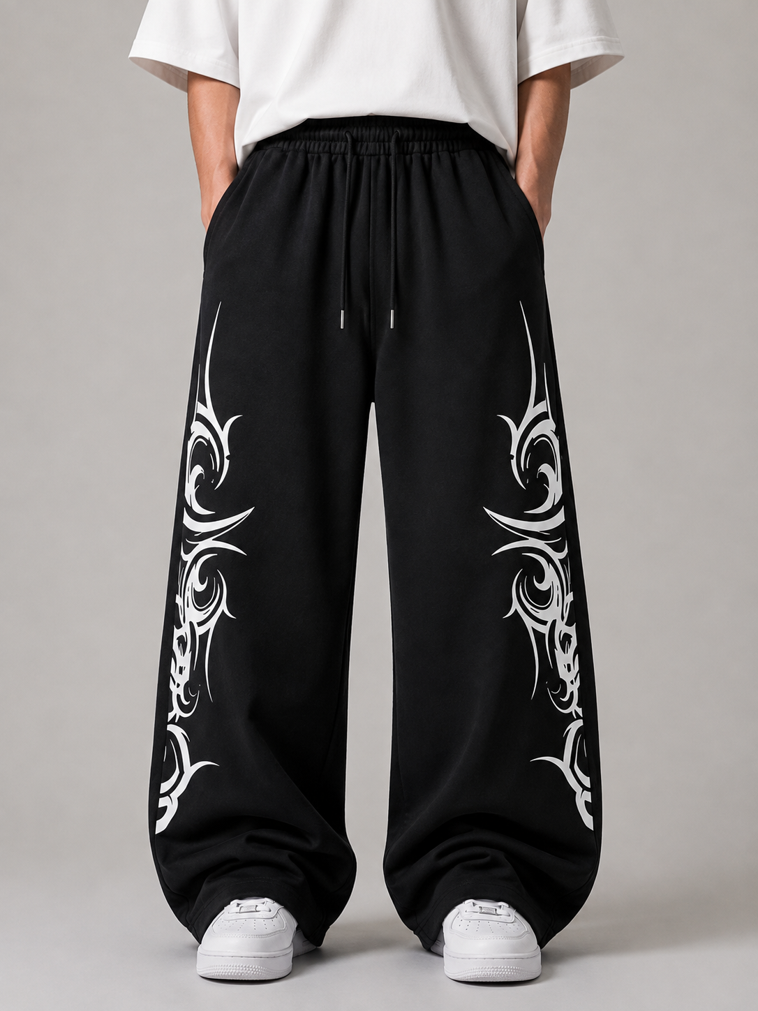 Black wide-leg sweatpants with white tribal-style graphic prints on both legs, shown on a model wearing a white t-shirt and white sneakers against a neutral gray background.