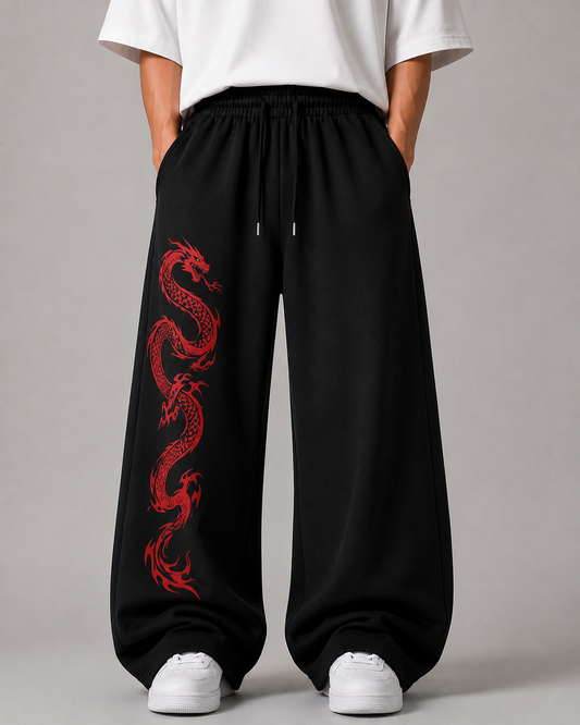 Black wide-leg sweatpants with a red dragon graphic printed down the left leg, worn by a model with a white t-shirt and white sneakers against a gray studio background.