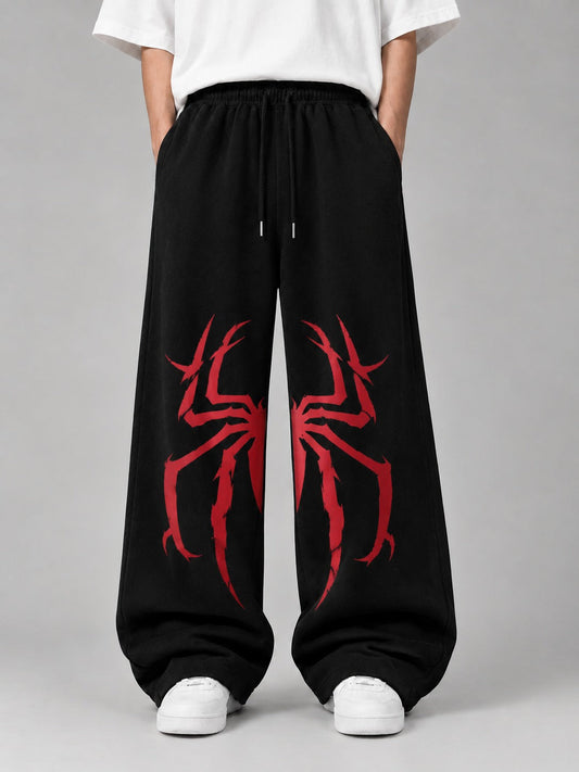 Black wide-leg sweatpants with a large red spider graphic on each leg, shown on a model wearing a white t-shirt and white sneakers against a gray studio background.