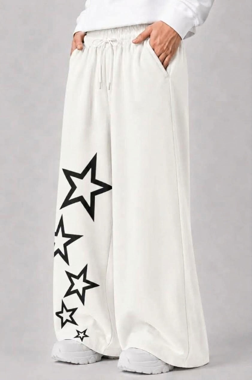 White wide-leg sweatpants with black outlined star graphics printed down one leg, shown on a model from the waist down against a light gray background.