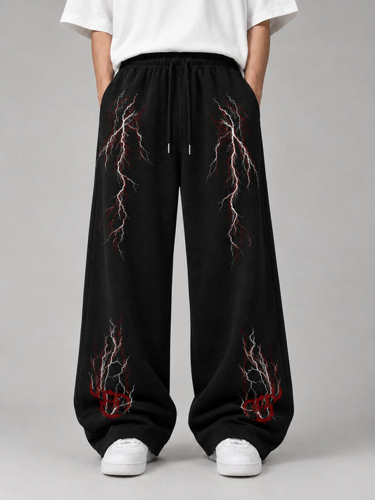 Black wide-leg sweatpants with red and white lightning bolt graphics, modeled with a white t-shirt and white sneakers against a gray studio background.