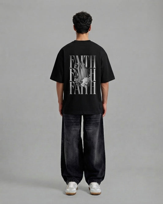 A man viewed from behind wearing a black t-shirt with a large white graphic print on the back, paired with dark wide-leg jeans and white sneakers, against a solid gray studio background.
