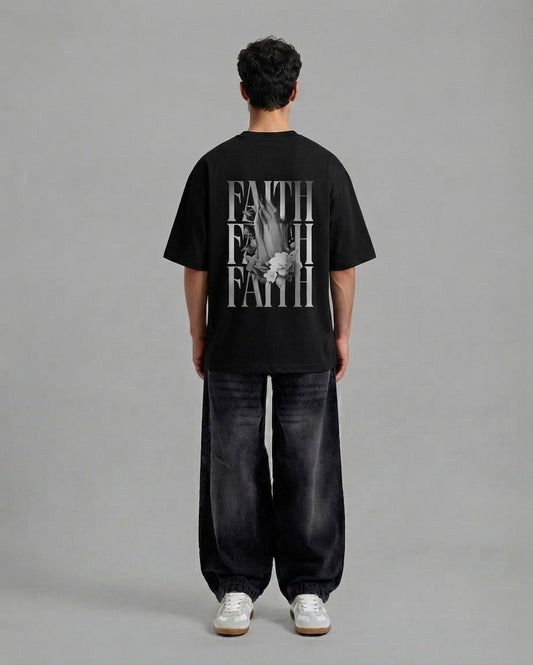 A man viewed from behind wearing a black t-shirt with a large white graphic print on the back, paired with dark wide-leg jeans and white sneakers, against a solid gray studio background.