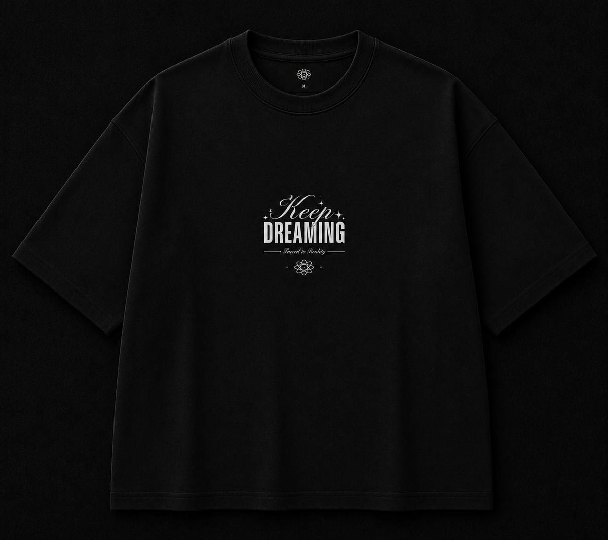 A black oversized short-sleeve t-shirt with a white graphic print on the chest reading 'Keep DREAMING' in stylized lettering, displayed flat against a solid black background.