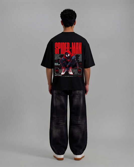 A man viewed from behind wearing a black Spider-Man graphic t-shirt and wide-leg black pants, standing against a neutral gray studio background.