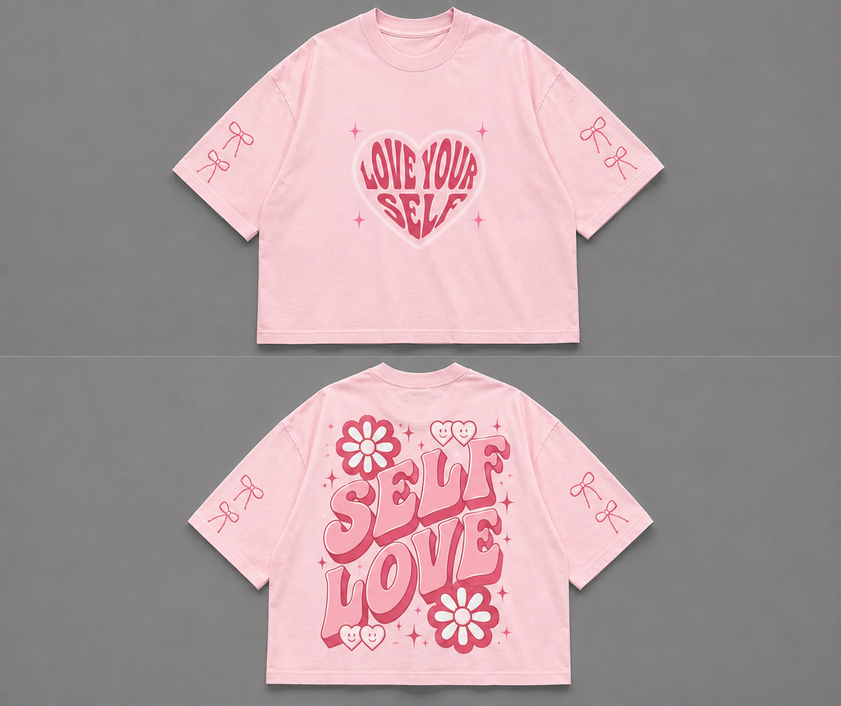 A light pink cropped t-shirt shown from both the front and back against a solid gray background. The front features a central pink heart graphic with the words 'LOVE YOUR SELF' in stylized lettering, and 'LOVE' is also written vertically on the back in large pink letters, decorated with flowers and hearts.