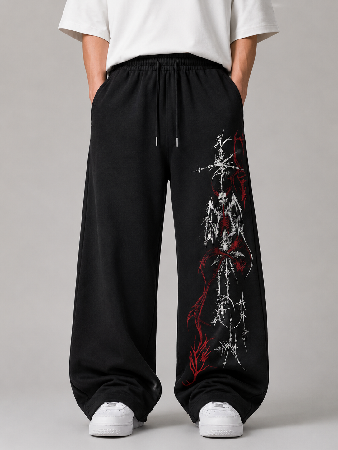 Black wide-leg sweatpants with a red and white graphic print on the right leg, worn by a model with a white t-shirt and white sneakers against a gray studio background.