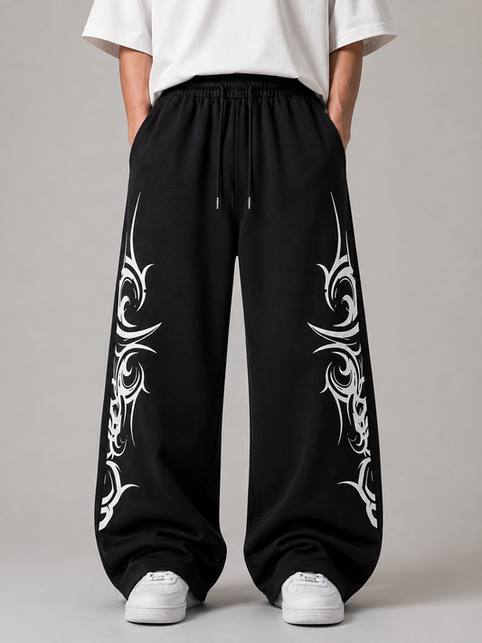 Black wide-leg sweatpants with white tribal-style graphic prints on both legs, shown on a model wearing a white t-shirt and white sneakers against a neutral gray background.