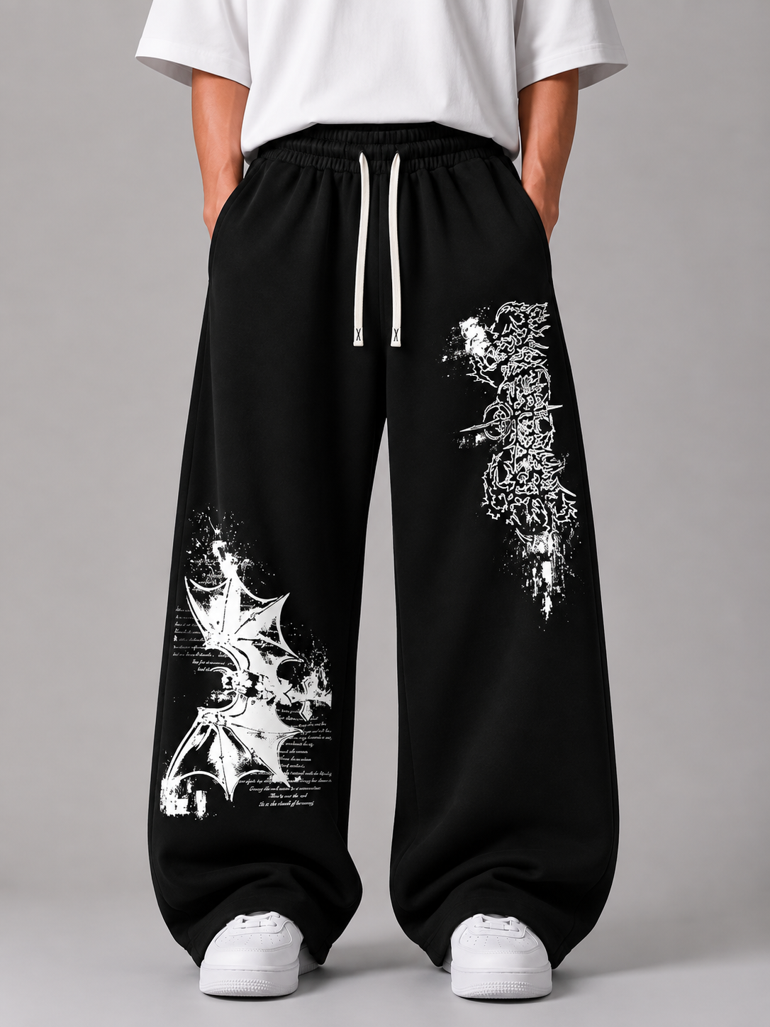Black wide-leg sweatpants with white graphic prints of a winged creature and gothic text, shown on a model wearing a white t-shirt and white sneakers against a gray studio background.