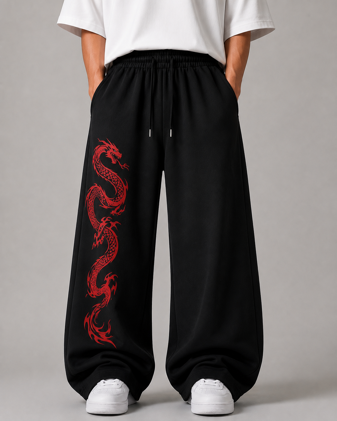Black wide-leg sweatpants with a red dragon graphic printed down the left leg, worn by a model with a white t-shirt and white sneakers against a gray studio background.