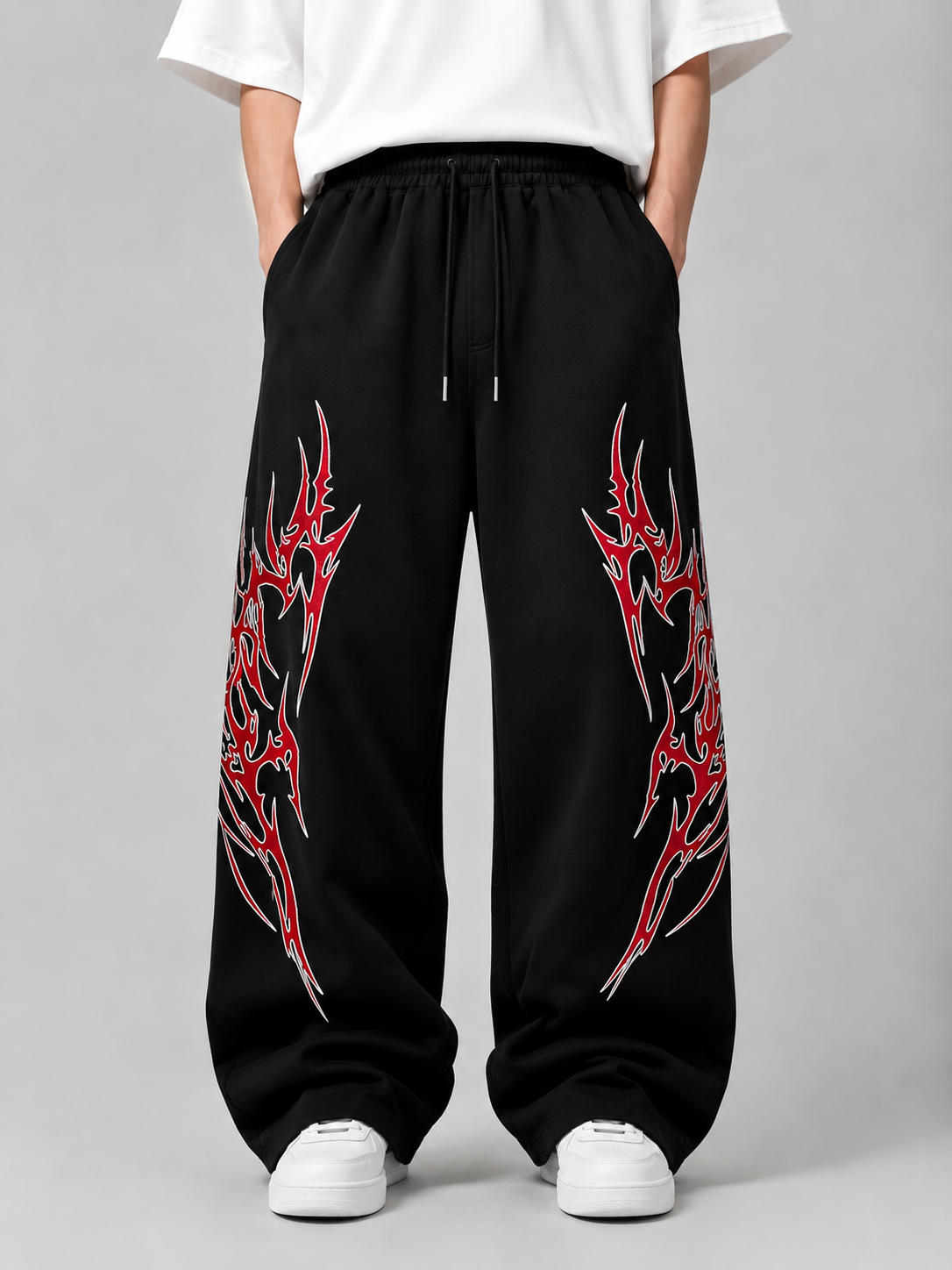 Black wide-leg sweatpants with red and silver tribal-style graphic prints on both legs, shown on a model wearing a white t-shirt and white sneakers against a gray studio background.