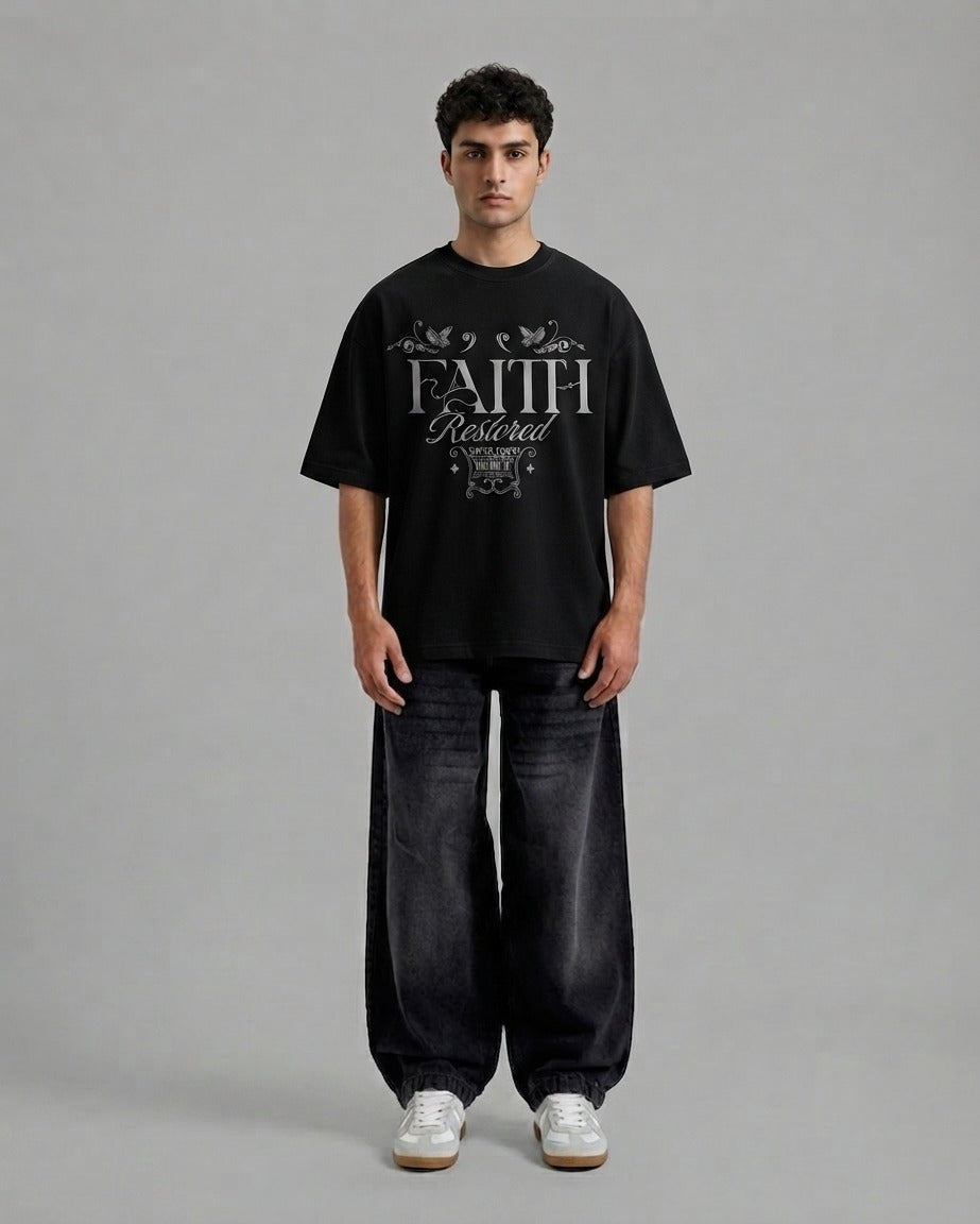 A man stands against a plain gray studio background wearing a black oversized T-shirt with a large white 'FAITH Protected' graphic on the front, loose dark jeans, and white sneakers.