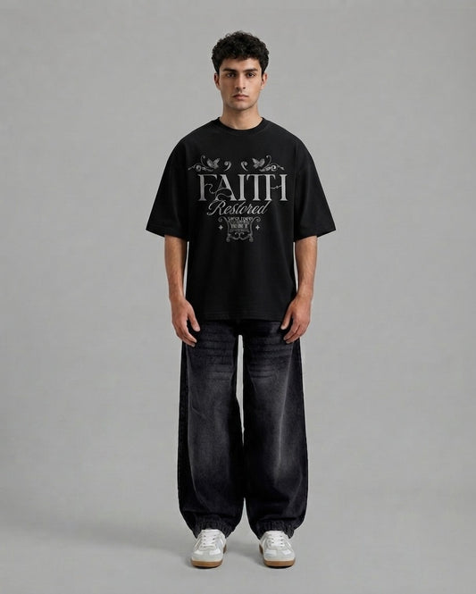 A man stands against a plain gray studio background wearing a black oversized T-shirt with a large white 'FAITH Protected' graphic on the front, loose dark jeans, and white sneakers.