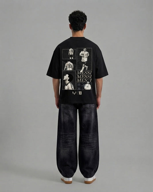 A model viewed from the back wearing a black t-shirt with a large white and gray Messi graphic print on the back, paired with dark wide-leg jeans, against a solid gray studio background.
