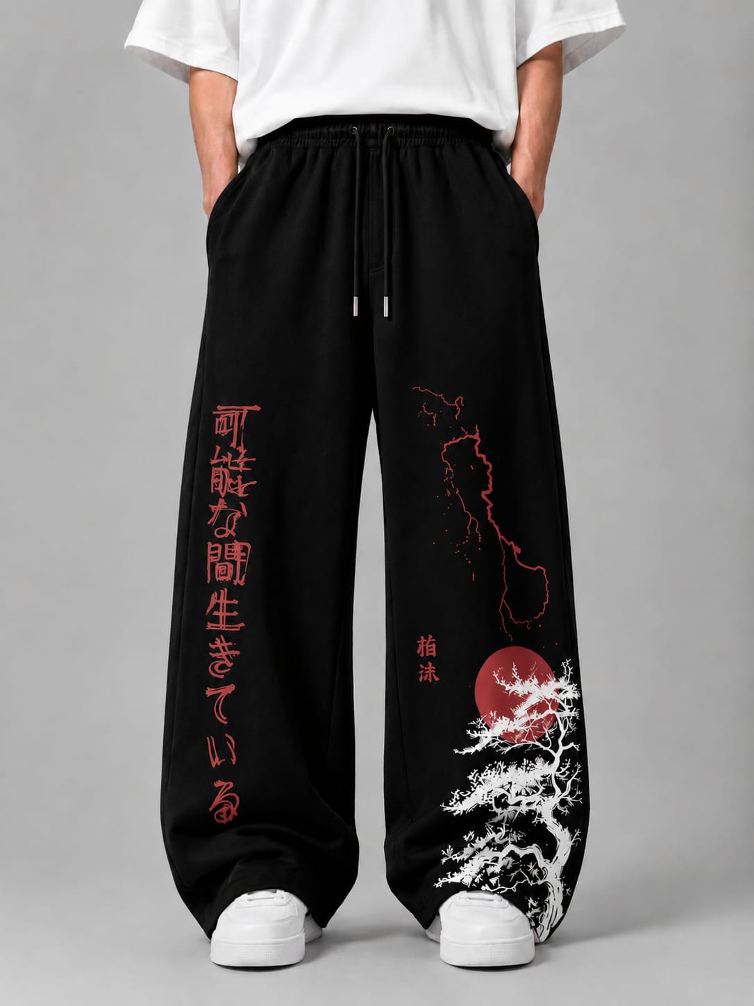 Black wide-leg sweatpants with red Japanese text and red/white graphic prints, shown on a model wearing a white t-shirt and white sneakers against a gray studio background.