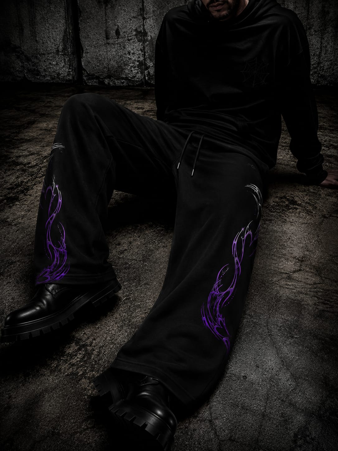 Black wide-leg gothic pants featuring purple flame-style graphics on both legs, styled with black boots in a dark industrial setting.
