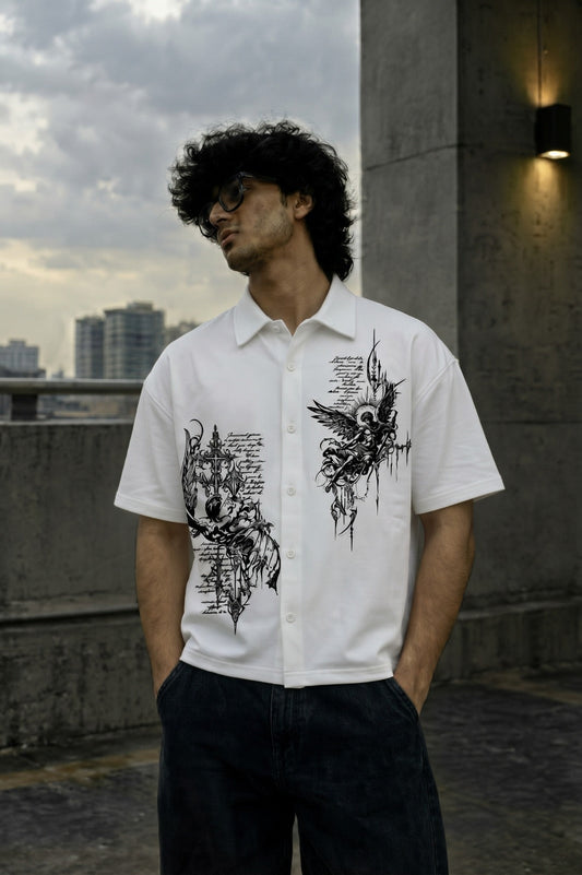 A man wearing a white short-sleeve button-up shirt with black graphic prints, standing on a concrete rooftop with a city skyline in the background.