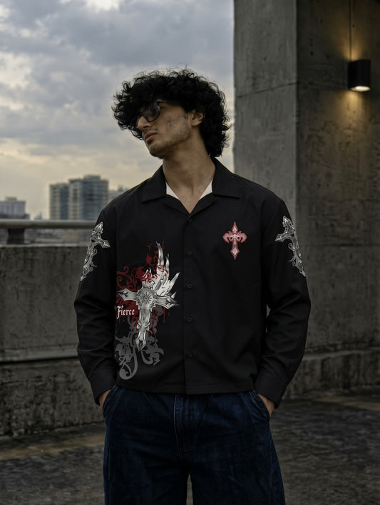 A man wearing a black button-up shirt with detailed red, white, and silver dragon graphics on the front and sleeves, paired with dark blue jeans, standing outdoors against a concrete wall and cloudy sky.