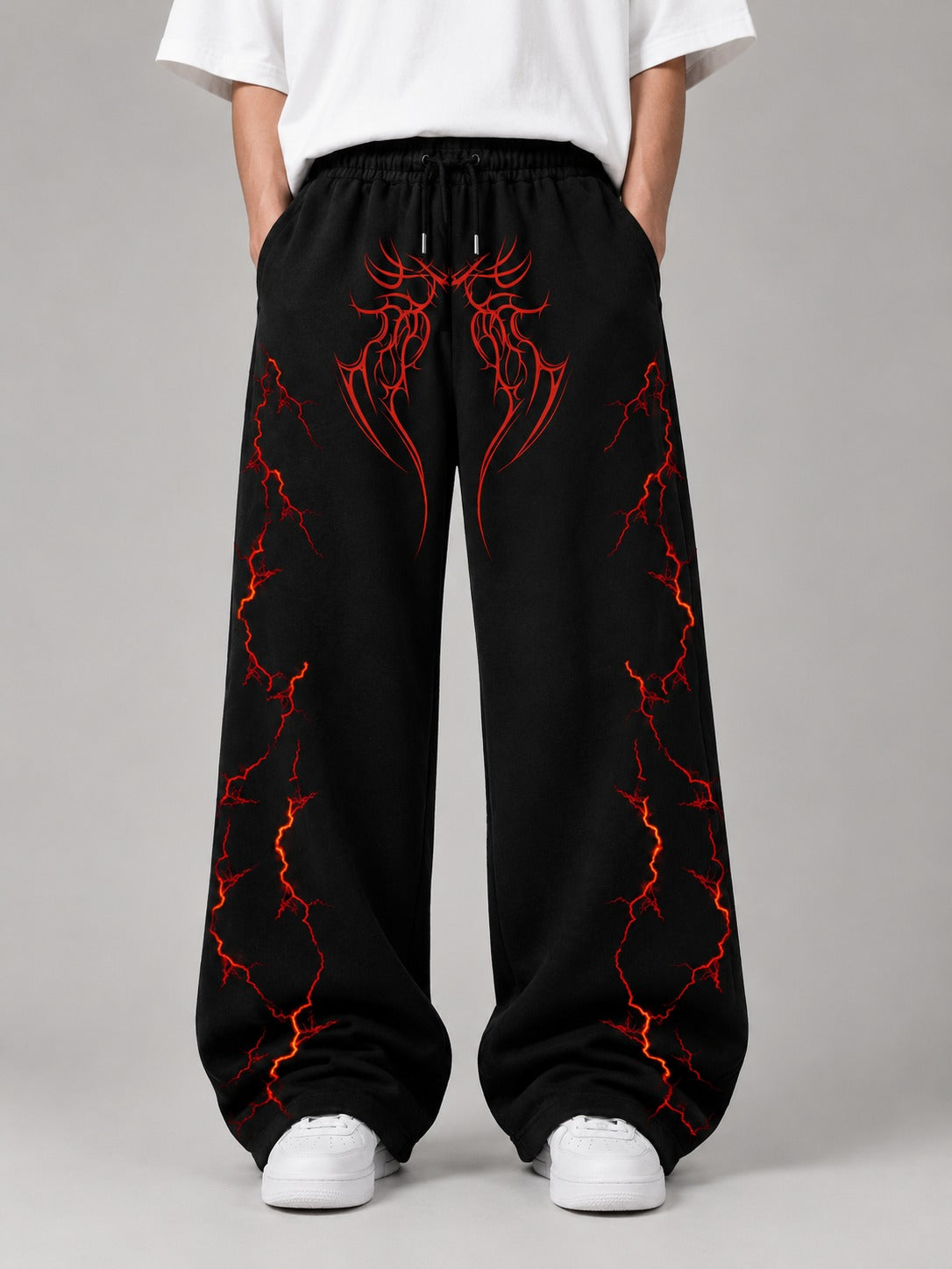 Black wide-leg sweatpants with a red and orange lightning-bolt graphic pattern, modeled with a white t-shirt and white sneakers against a gray studio background.