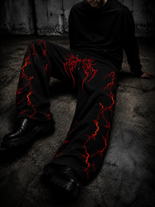 A person wearing black wide-leg pants with a vivid red lightning-bolt graphic pattern, seated on a dark concrete floor.