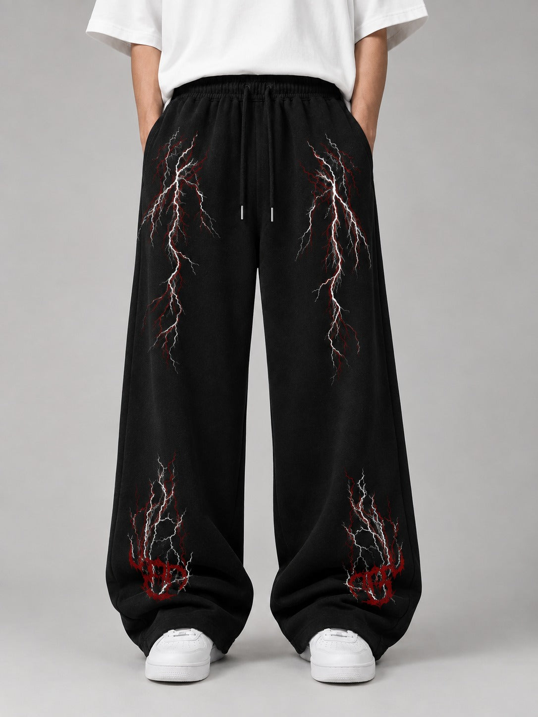 Black wide-leg sweatpants with red and white lightning bolt graphics, modeled with a white t-shirt and white sneakers against a gray studio background.