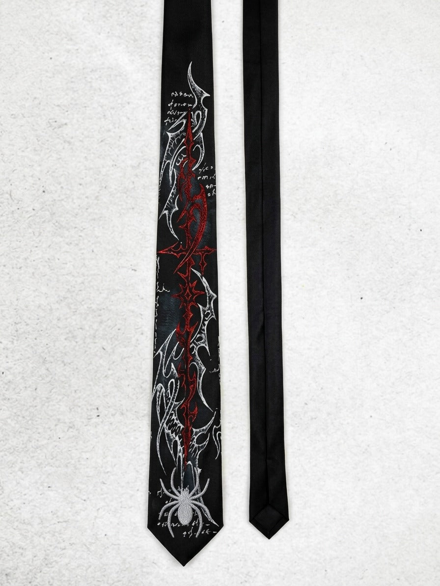 A black necktie with a detailed graphic print featuring a red cross, white spiderweb motifs, and gothic script, displayed next to a plain black necktie on a light gray textured background.