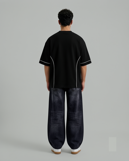 Black oversized short-sleeve shirt with white piping details along the sleeves and sides, paired with dark wide-leg jeans, shown from the back on a male model.