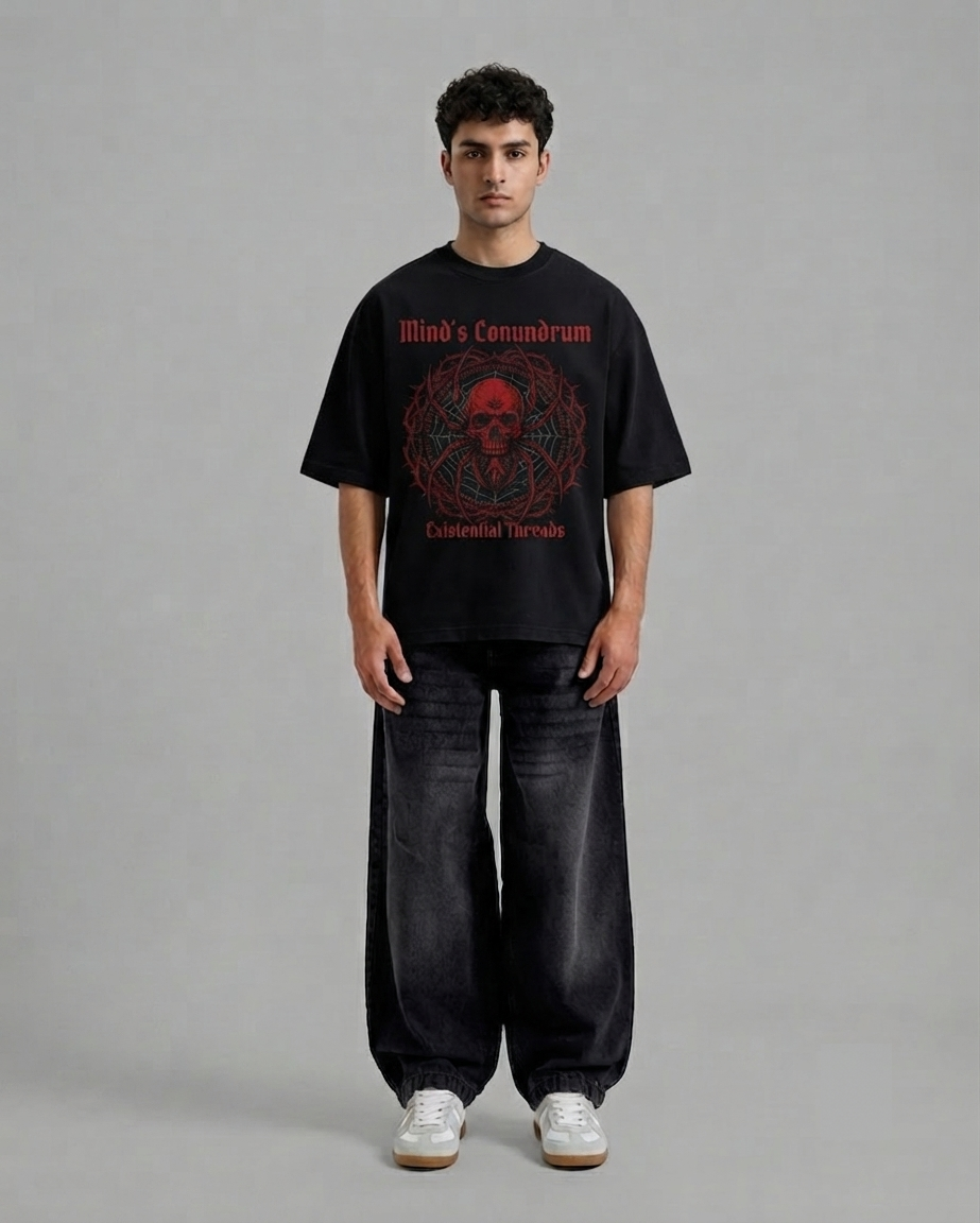 A man modeling a black graphic t-shirt with a red circular skull design and the text 'Mind's Communion' and 'Existential Terrorism'. He is wearing baggy dark jeans and white sneakers against a plain gray studio background.